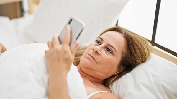 Латиноамериканка Средних Лет Выглядящая Смартфон Лежит Кровати Спальне — стоковое фото