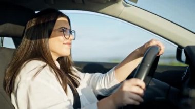 Genç, güzel, İspanyol bir kadın araba kullanıyor, dans ediyor, işaret diliyle şarkı söylüyor.