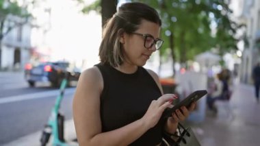Neşeli İspanyol kadın neşe içinde Madrid 'in canlı caddelerinde akıllı telefon kullanıyor. Gözlükleri şehrin çekiciliğini yansıtıyor. Muhteşem gülümsemesi cep telefonunda sohbet ediyor..