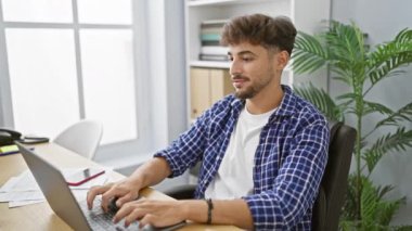 Gülümseyen, kendine güvenen genç bir Arap ofisteki dizüstü bilgisayarı üzerinde sevinçle çalışıyor başarılı bir yönetici olarak pozitif enerji yayıyor.
