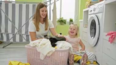 Kafkasyalı mutlu anne ve kız ev işleri üzerinde kaynaşıyor, çamaşır odasında yerde birlikte oturuyor, bir sepet dolusu kıyafet tutuyorlar.
