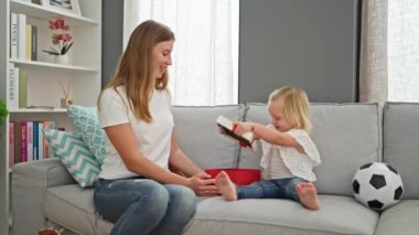 Beyaz bir anne ve kızın evde birlikte bir doğum günü hediyesi açması, sıcak gülümsemeleri odayı aydınlatıyor.