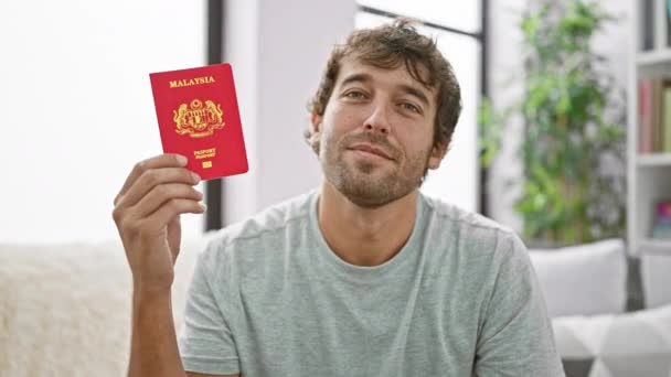 Jovem Bonito Sorrindo Alegria Sentado Sofá Casa Segurando Seu Passaporte — Vídeo de Stock
