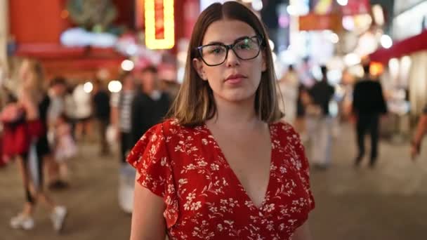 美しいヒスパニック女性 メガネの背後にある深刻な表現は 夜に大阪のドトンボリ通りに単独で立っています 都市ライトの下の都市観光客の光景 — ストック動画