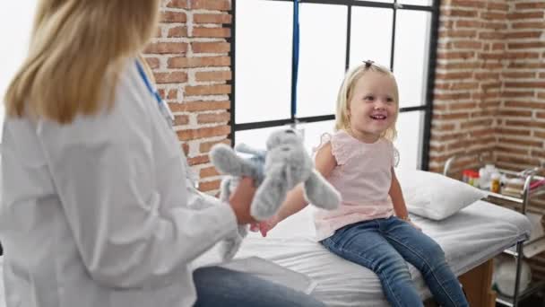 小児クリニックでウサギのおもちゃを持つ幸せな子供患者 自信を持った女性医師と楽しい診察を受ける — ストック動画