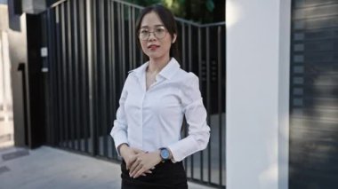 Şehirde poz veren, gözlüklü, kendine güvenen Asyalı iş kadını.