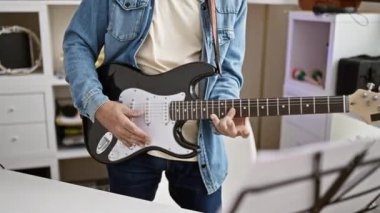 Modern bir evde elektro gitar çalan olgun bir adam, evde müzik tutkusu ve eğlence aktivitesi sergiliyor.