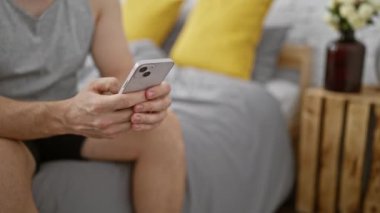 Sarı aksanlı ve kırsal komodinli rahat bir yatak odasında akıllı telefon kullanan yakışıklı bir adam..