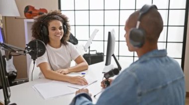 Canlı yayında yumruk tokuşturan iki gülümseyen muhabir, stüdyoda yapılan radyo röportajında elde edilen başarıyı kutluyor..