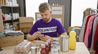 Gönüllü tişörtlü sakallı genç bir adam depoda bağış toplarken yiyecekleri inceliyor..