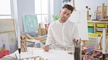 Genç, yakışıklı İspanyol bir adam hevesle kağıda resim çiziyor, sanatına dalmış ve vızıldayan bir stüdyoda konsantre olmuş.