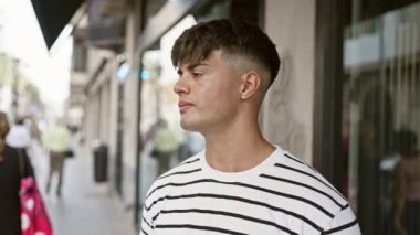 Serin, rahat İspanyol genç adam, güneşli şehir caddesinde dikilirken ciddi bir ifadeyi resmediyor, şehir yaşam tarzını özümsüyor..