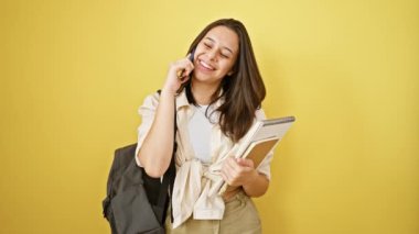 Kendine güveni tam genç İspanyol bir kız öğrenci, telefonda neşeli bir şekilde konuşuyor, sarı arka planda tek başına duruyor, kitapları akıllıca çeviriyor, ışıl ışıl bir gülümsemeyle gündelik, eğlenceli yaşam tarzını sergiliyor..