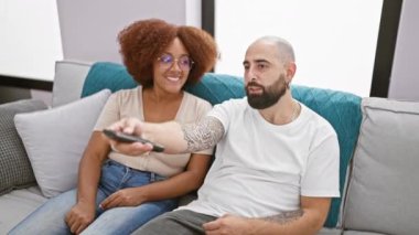 Hoş, ırklar arası bir çiftin kapalı mekanda uzaktan kumanda savaşı rahat oturma odalarında oturup, iyi huylu televizyon kanallarının kavgalarını değiştirirken.