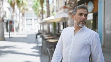 Endişeli, gri saçlı, sakallı, şehir sokağında durmuş ciddi bir yüzle kol saatini kontrol eden İspanyol genç adam geç mi kaldı??