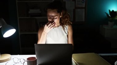 Odaklanmış beyaz bir kadın loş bir ofiste geç saatlere kadar çalışıyor, gözleri dizüstü bilgisayarının ekranında..