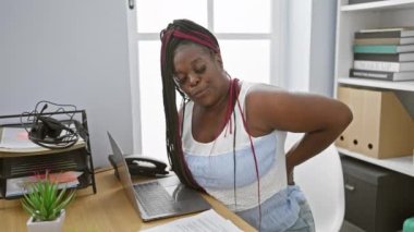 Mutsuz Afro-Amerikan iş kadını ofis masasında otururken sırt ağrısı çekiyor.