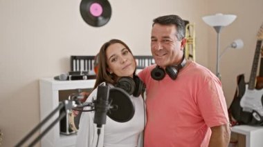 Müzik stüdyosunda müzik aleti çalarken birlikte gülümseyen, kulaklık takan kendine güvenen erkek ve kadın müzisyenler.