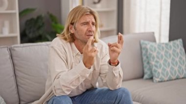 Oturma odasında kanepede parmaklarını çaprazlayan endişeli adam zaferi kollarını kaldırarak kutluyor..