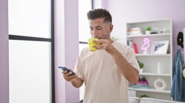 Çekici, genç İspanyol bir adam. Dikkatle telefonunu kullanıyor. Evinin rahat ortamında sıcak espresso içiyor.