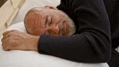 Sakallı kel bir adam yastığın üzerinde dinleniyor. Rahatlık ve rahatlık gösteriyor..