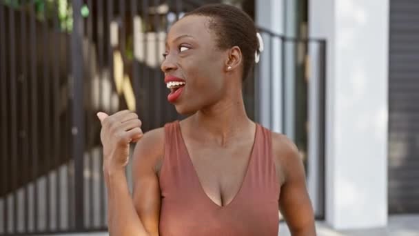 市街地に立っている喜びのアフリカ系アメリカ人女性は 明るく開いた笑顔で親指を向ける — ストック動画