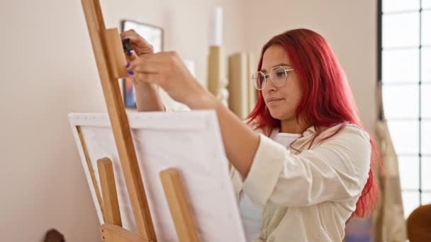 クリエイティビティを引き出す準備をしている自信のある若い赤毛の女性アーティスト 居心地の良いアートスタジオで描くためにイーゼルに空白のキャンバスを置く — ストック動画