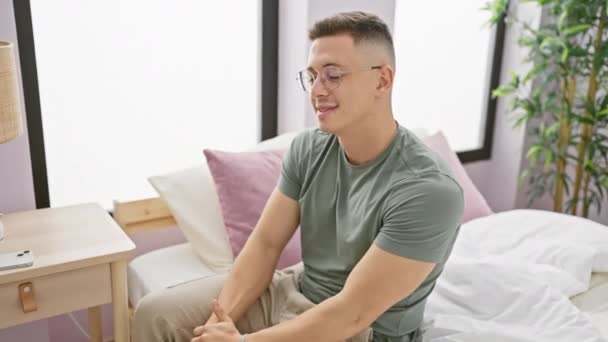 Sonriente Joven Hispano Con Gafas Sentadas Casualmente Dormitorio Con Interior — Vídeos de Stock