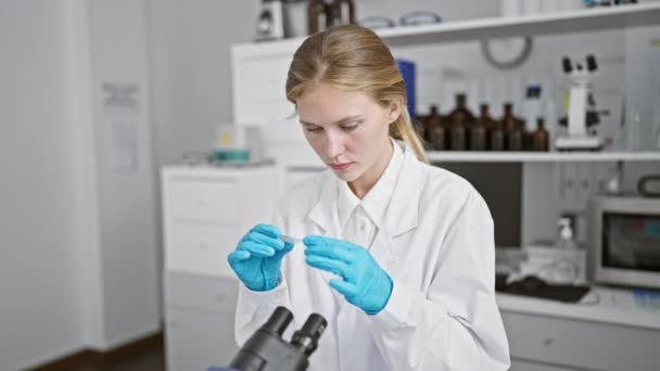 一位穿着白色实验室外套的专注的年轻女性在临床实验室的显微镜下检查样本 — 图库视频影像