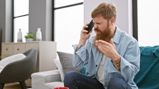 坐在客厅里的爱尔兰红头发男人 一边用智能手机强调自己的谈话 一边沮丧地 绝望地战斗着 — 图库视频影像