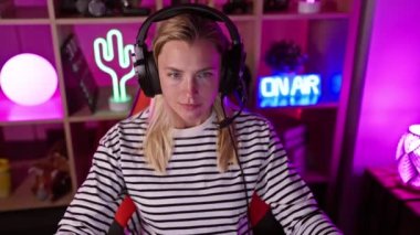 Gece vakti neon ışıklı oyun odasında gülümseyen kulaklıklı sarışın kadın.