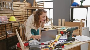 Genç, çekici bayan marangoz atölyesinde dizüstü bilgisayar ve akıllı telefon kullanarak çevrimiçi sohbete daldı.