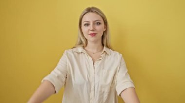 Neşeli genç sarışın kadın ellerini ve parmaklarını yaratıcılık ve hayal gücüyle kullanarak resim çerçevesi oluşturuyor. Canlı sarı izole bir arkaplanda mutlu anları yakalamak..