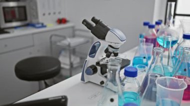 Laboratuvar masasında oturan odaklanmış genç sarışın bilim kadını mikroskop kullanarak ciddi tıbbi araştırmalara daldı.