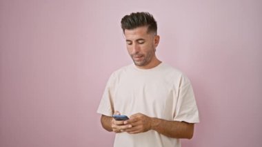 Kendine güveni tam, genç İspanyol bir adam canlı video görüşmesinden hoşlanıyor. Akıllı telefonuyla gülümsüyor. Canlı, pembe bir duvar arkasında izole edilmiş.
