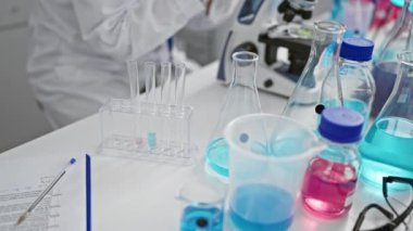 Kendini adamış genç kızıl saçlı bilim adamı, son teknoloji tıbbi araştırmalara dalmış, test tüpündeki sıvıyı uzmanca ölçüyor koruyucu gözlük ve eldivenlerle güvenliği sağlıyor..