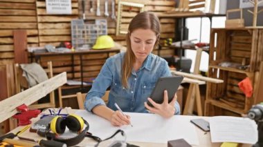 Marangozluk atölyesinde proje planlaması için tablet kullanan odaklanmış genç bir kadın