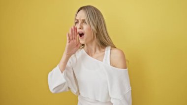 Hiçbir şeyden haberi olmayan sarışın bir kadın, omuz silkmiş, 'Bilmiyorum' diyen bir omuz, sarı izole edilmiş arka planda şüpheli bir yüz, şaşkınlık içinde duran.