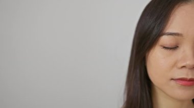 Huzurlu bir ifadeyle genç bir Asyalı kadın beyaz izole bir arka planda duruyor, sakinlik ve basitliği çağrıştırıyor..