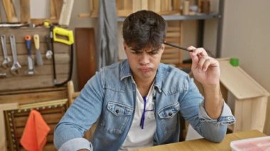 Stresli genç bir İspanyol, profesyonel bir marangoz, iş yerindeki problemden dolayı üzgün, marangozluk atölyesinde oturuyor, defteri açık..