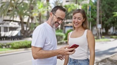 Kendine güveni tam bir baba-kız güzel bir anı paylaşıyorlar, neşeli bir şekilde cep telefonlarında serin bir selfie çekiyorlar hareketli bir şehir caddesinde duruyorlar..