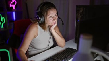 Yorgun genç sarışın flamalı kadın, karanlık oyun odasında gece baykuşu, fütüristik teknoloji ile akış ve oyun dünyasına gömülmüş.