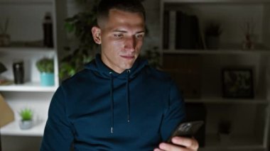 Modern ofis ortamında elinde akıllı telefon ve beyaz maske tutan kapüşonlu genç bir İspanyol.