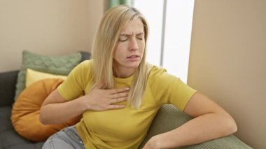 Sarışın kadın kendini iyi hissetmiyor. Eli göğsünde, koltukta oturuyor.