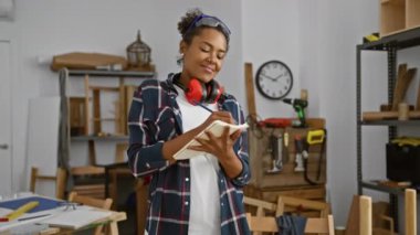 Etrafı aletlerle çevrili bir kadın, iyi donanımlı bir marangozluk atölyesinde notlar alır..