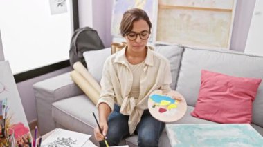 Rahatlamış genç İspanyol kadın, sanatsal bir şekilde kanepede meditasyon yapıyor, gözleri kapalı.