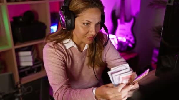 夜のゲームルームでコロンビアペソを数えるヘッドフォンを持つヒスパニック女性を笑う — ストック動画