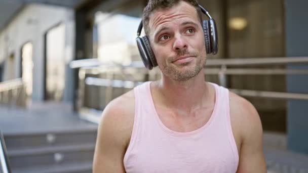 Egy Töprengő Szakállas Férfi Rózsaszín Felsőt Visel Fejhallgatóval Város Utcáján — Stock videók