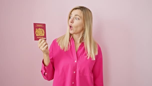 金发年轻女人 显然吓坏了 张大嘴地怀疑着 同时把她的北爱尔兰护照夹在孤立的粉色背景上 — 图库视频影像
