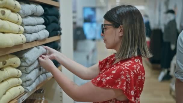 时尚激情 在零售店里 一个戴眼镜的漂亮女人在挑选时髦的衣服 在购物中心的一家精品店里 一个年轻的黑发购物者的画像 — 图库视频影像